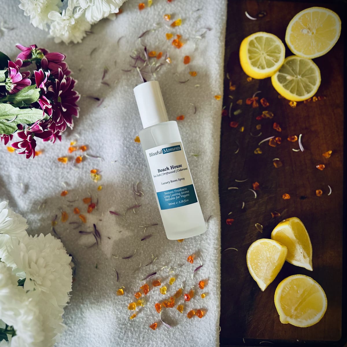 Beach House scented luxury frosted glass room spray surrounded by fresh flowers, amber and lemon sitting on a cosy blanket
