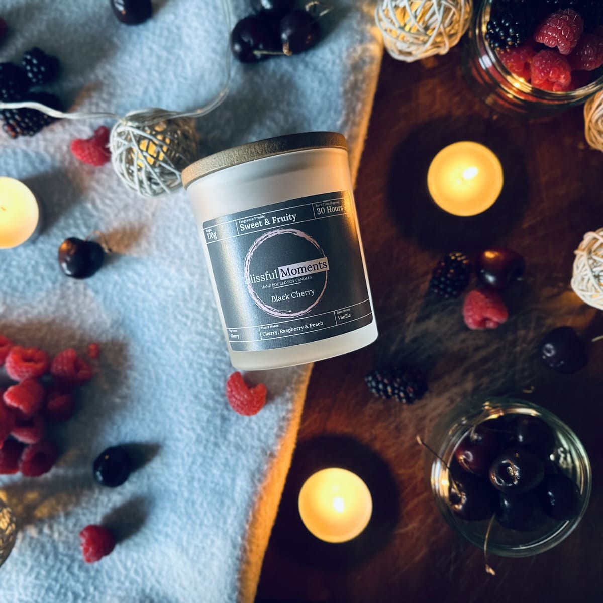 Fruity scetned soy wax candle surrounded by black cherries, raspberries and blackberries