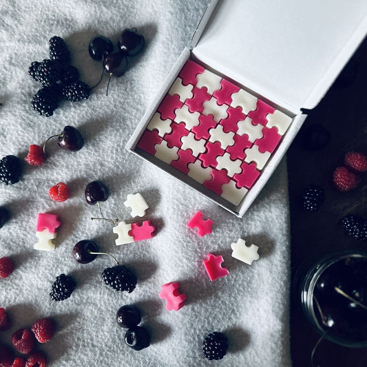 Fruity scented red and white puzzle shaped soy wax melts surrounded by black cherries, raspberries and blackberries