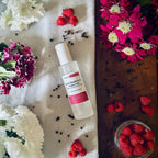 Black Raspberry & Peppercorn scented luxury frosted glass room spray surrounded by fresh flowers, peppercorns and raspberries sitting on a cosy blanket