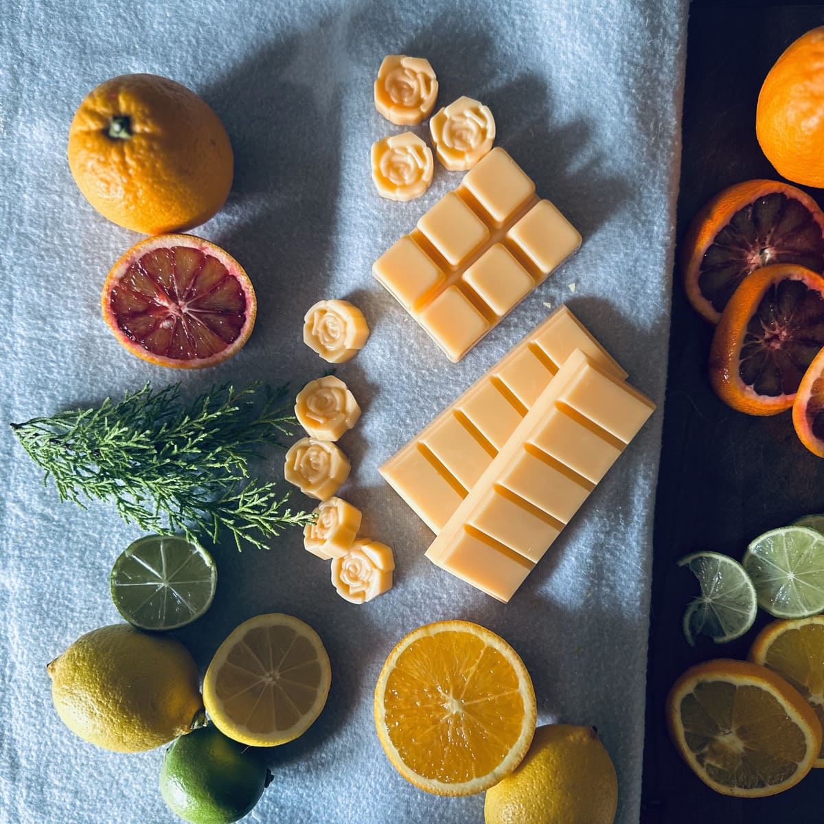 Orange coloured soy wax melts surrounded by blood oranges and citrus fruits