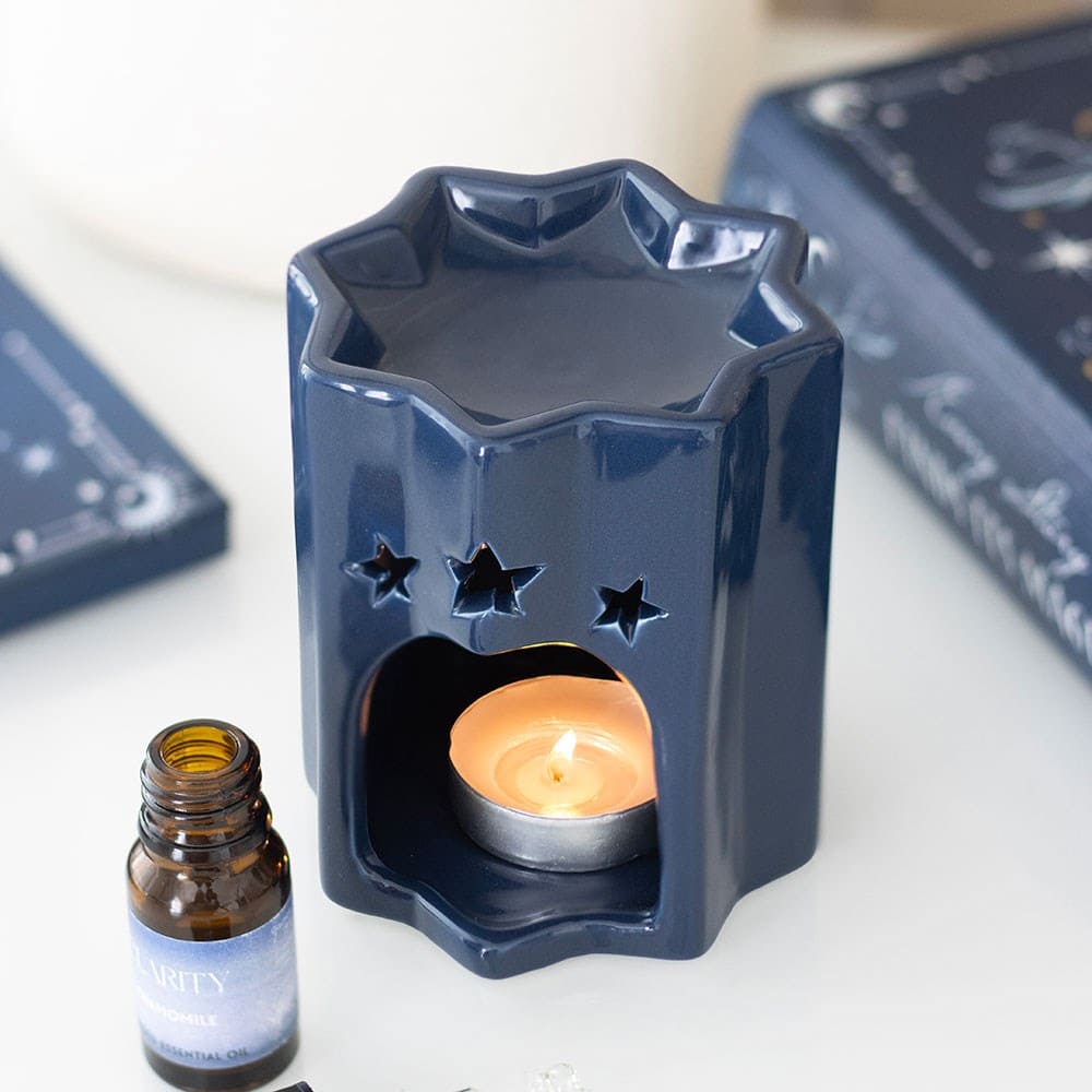 Navy blue star-shaped ceramic wax melt burner with a lit candle and a bottle of essential oil on a white surface.