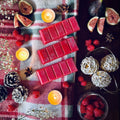 Red coloured Cherry and Fig scented snapbar wax melts on a festive checkered cloth with figs, tea lights, and raspberries around