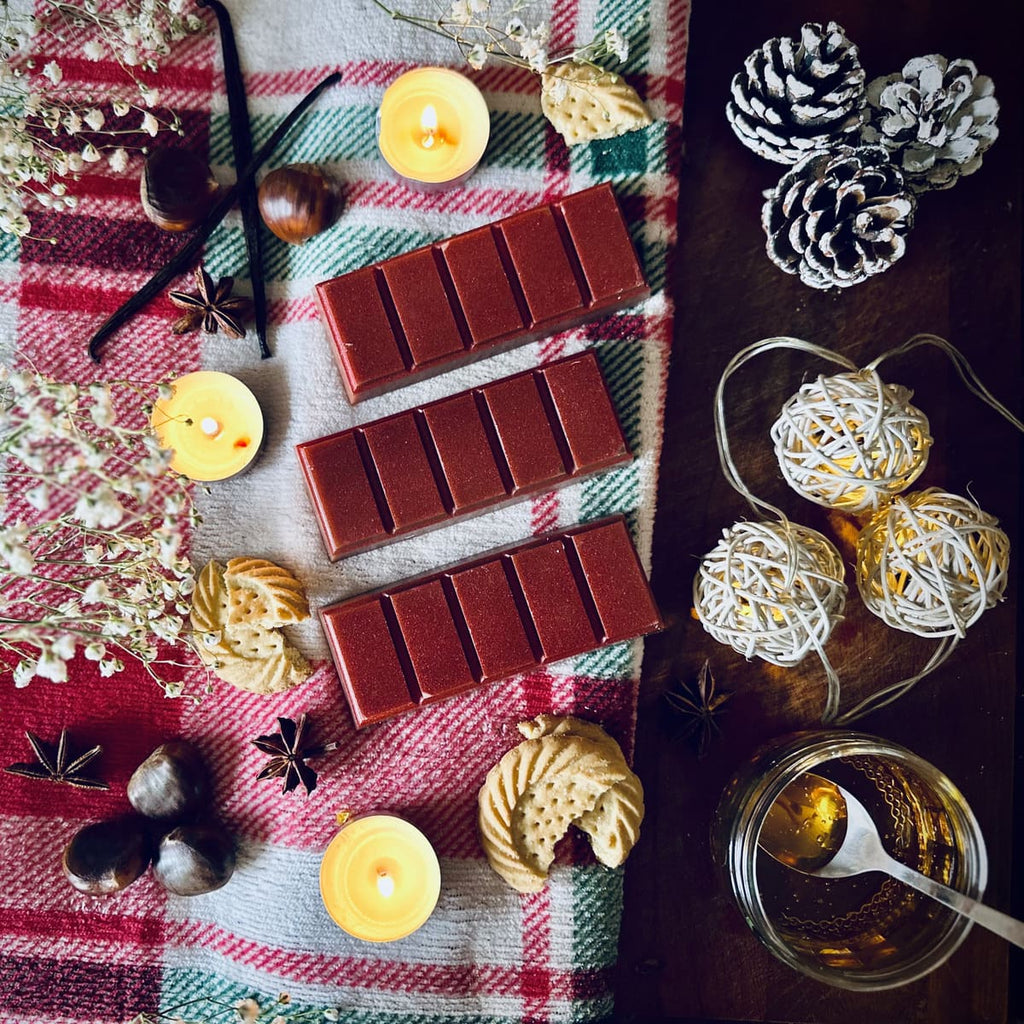 Christmas Cookies scented snapbar wax melts on a festive plaid cloth with tealights, chestnuts, pinecones, and decorative lights.