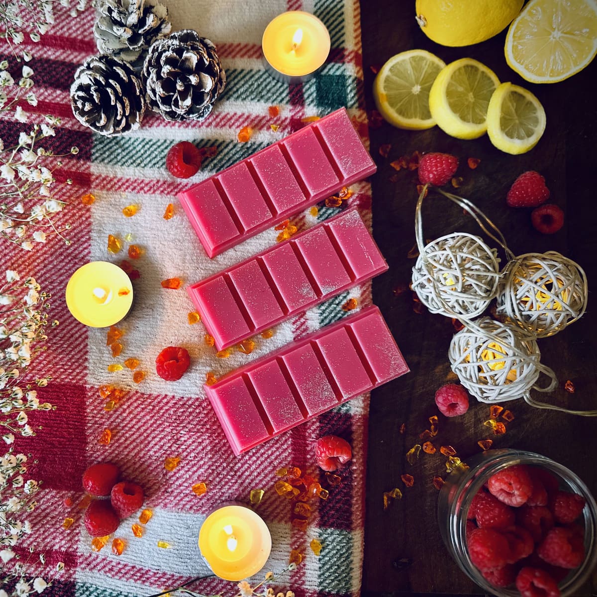 Red Christmas wish scented snpabar wax melts with silver glitter on a checkered cloth with candles, lemons, and raspberries.