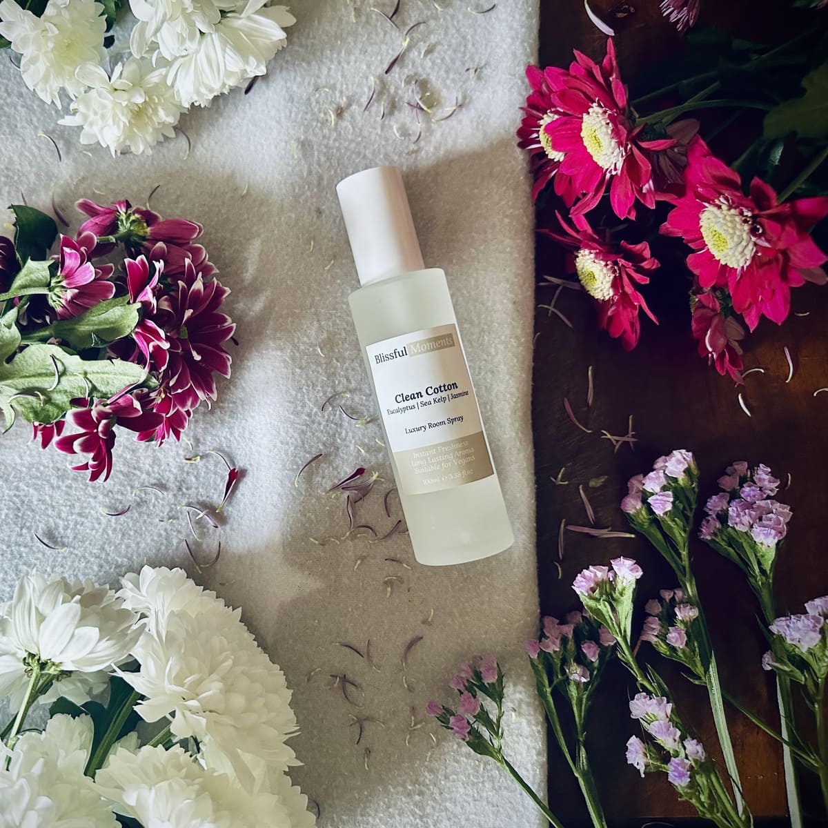 Luxury Clean Cotton scented room spray sitting on a soft cosy blanket surrounded by fresh flowers.