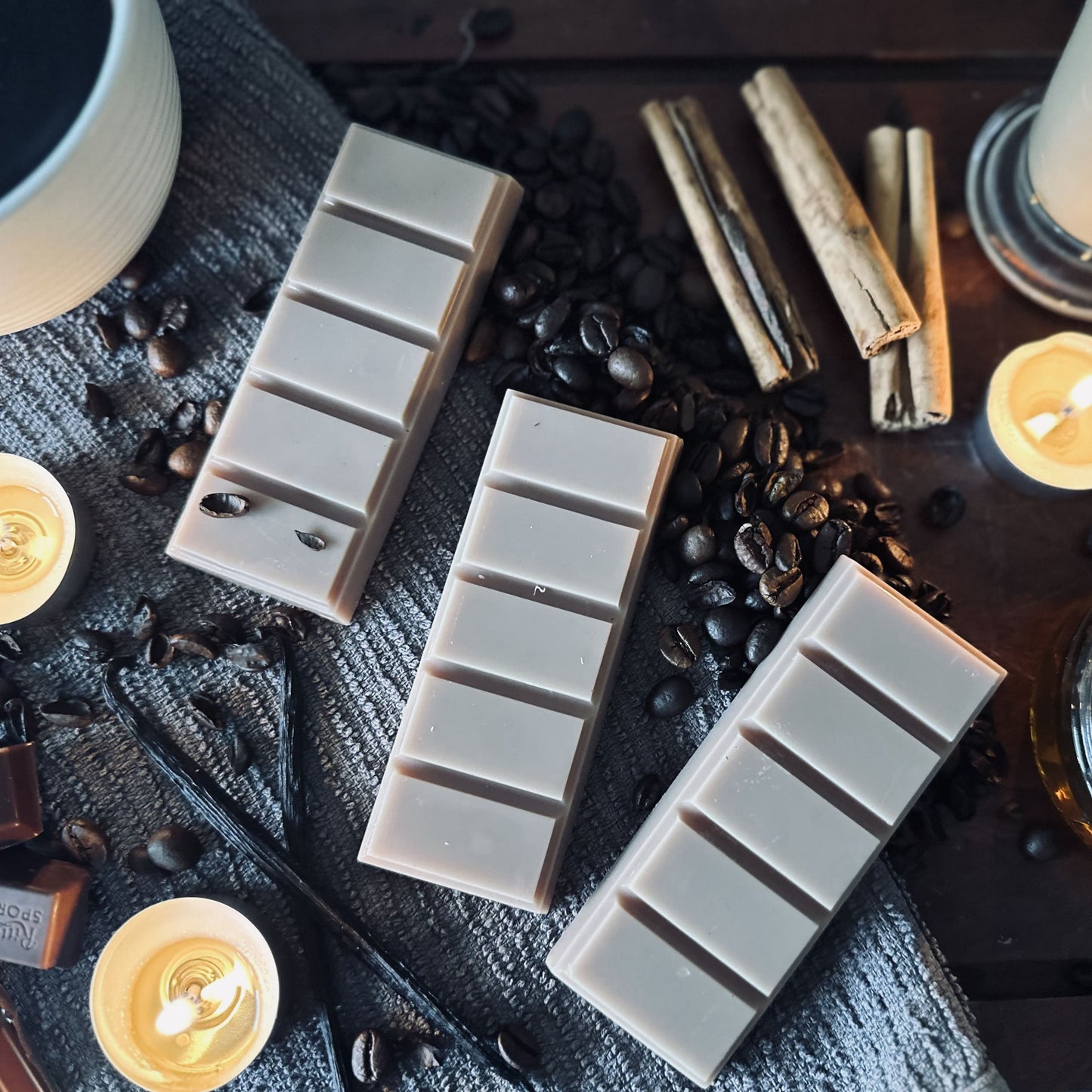 Brown soy wax melts sitting on coffee beans and surrounded by black coffee, cinnamon sticks and vanilla pods