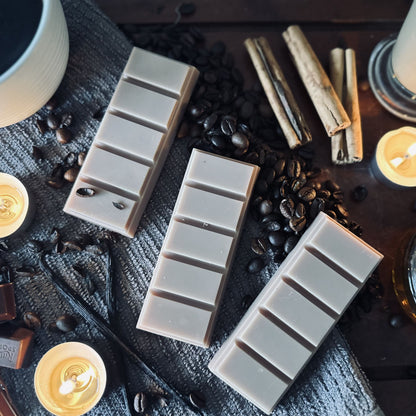 Brown soy wax melts sitting on coffee beans and surrounded by black coffee, cinnamon sticks and vanilla pods