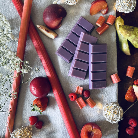 Fruity scented purple soy wax melts surrounded by fresh plums and rhubarb with other summer fruits