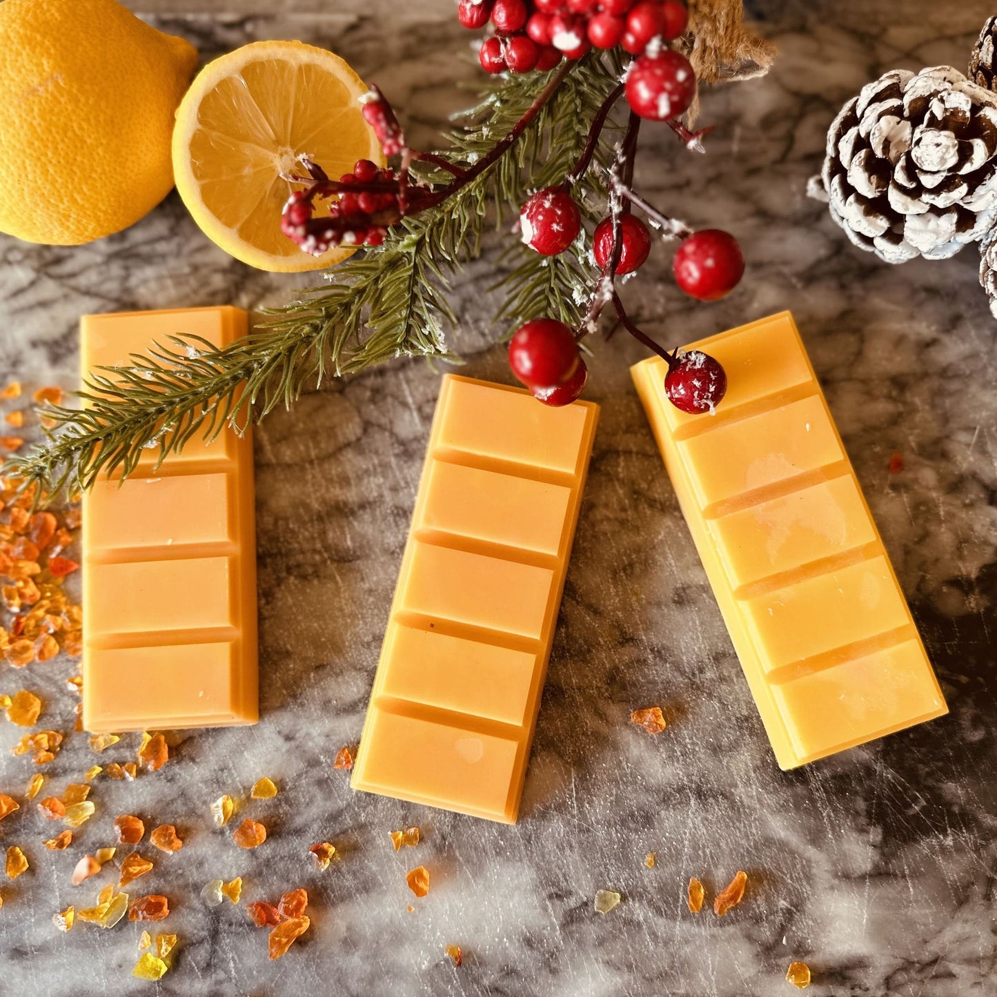 Orange coloured soy wax melts surrounded by amber, lemons and Christmas decorations 