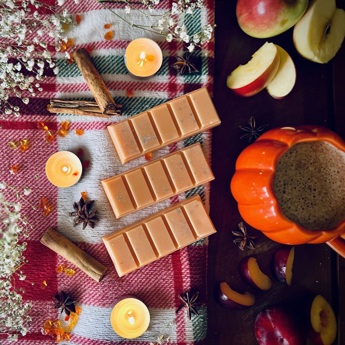 Orange Frosted Pumpkin scented snapbar wax melts on a red checked tablecloth surrounded by festive pumpkins, apples, plumbs and cinnamon
