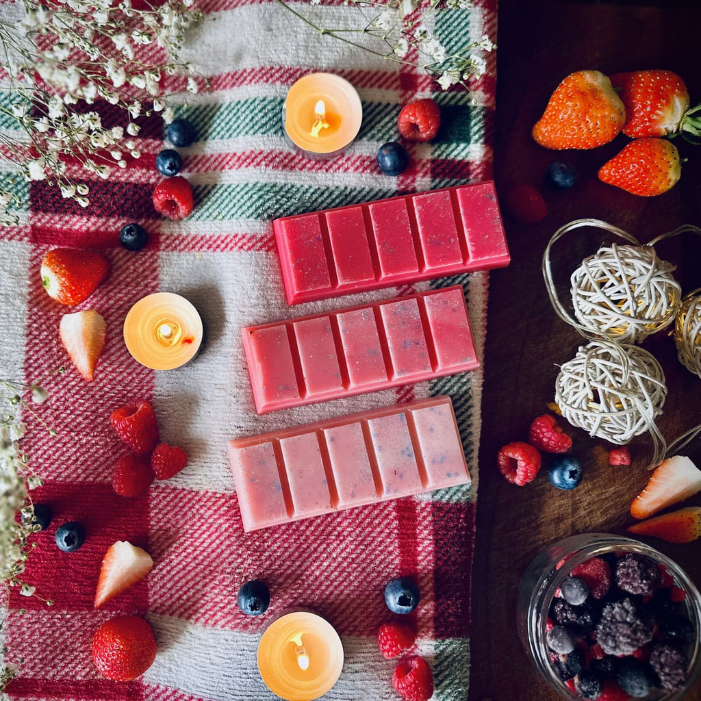Red coloured Frosty Berries snapbar wax melts on a checked plaid cloth with candles, winter berries, and fruits.