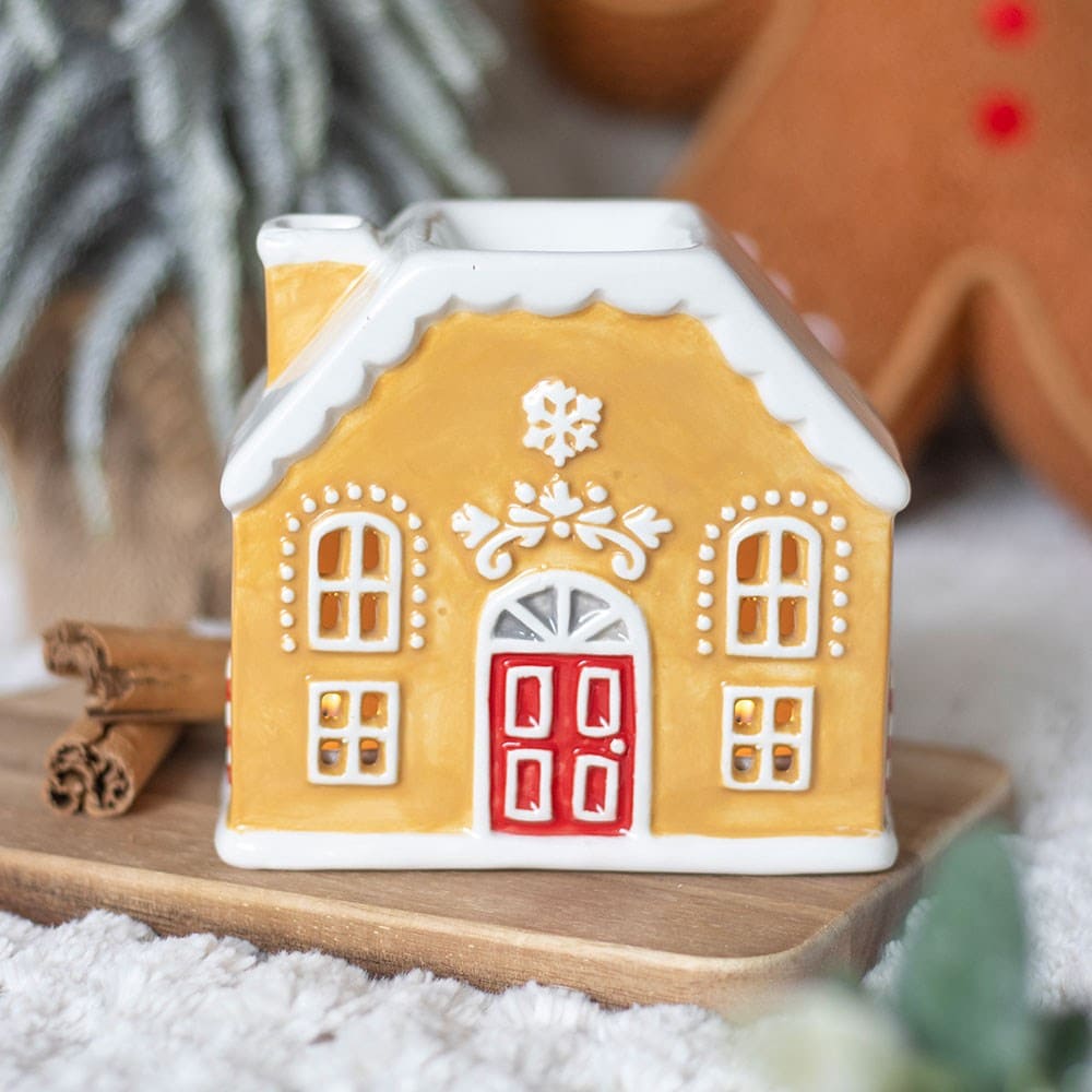 Gingerbread house shaped wax melt burner on a wooden board with cinnamon sticks in a festive winter setting