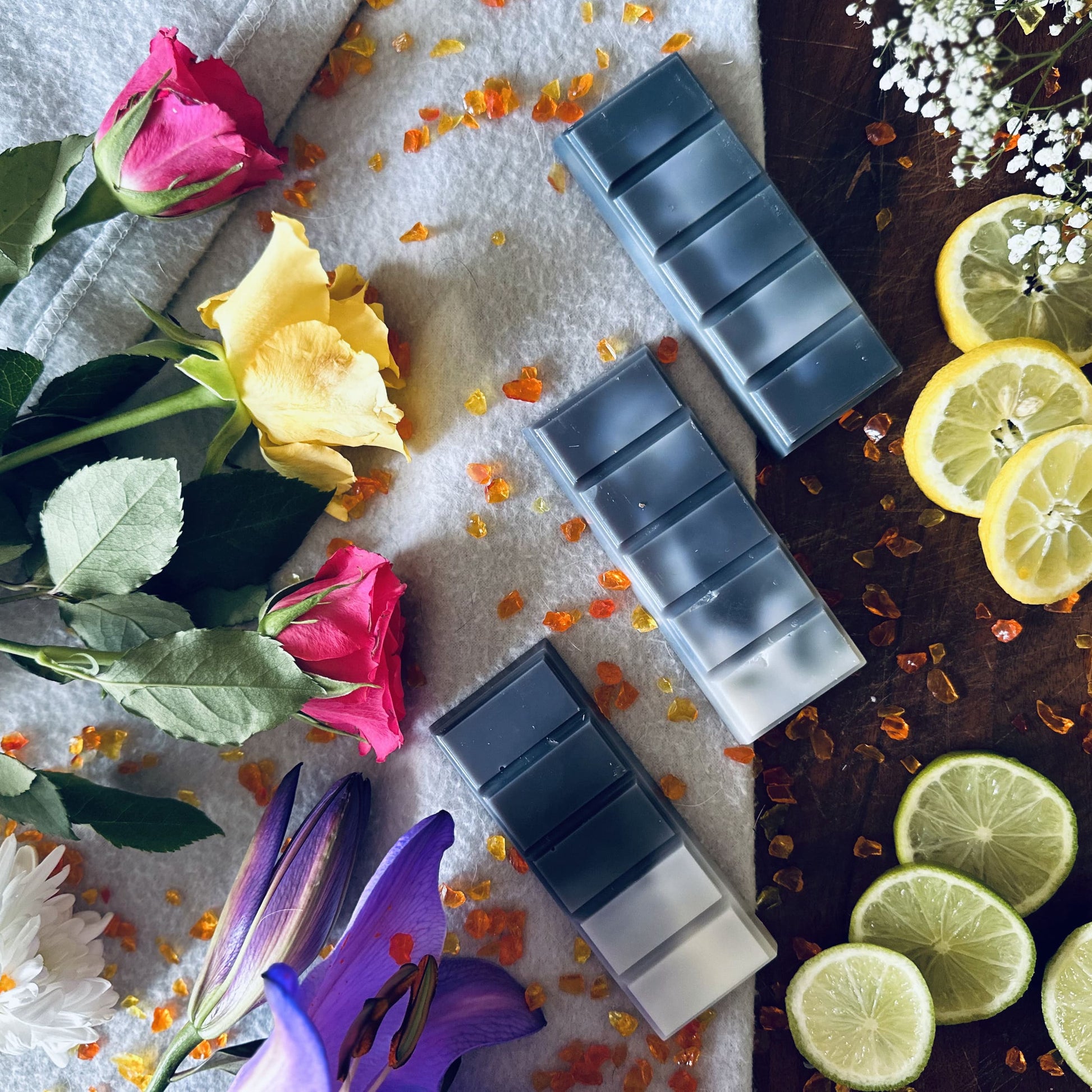 Black and white soy wax melts surrounded by floral roses, lilies and citrus fruits