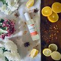 Luxury Mandarin & Clove scented rom spray surrounded by fresh flowers and citrus rooms sitting on a cosy blanket