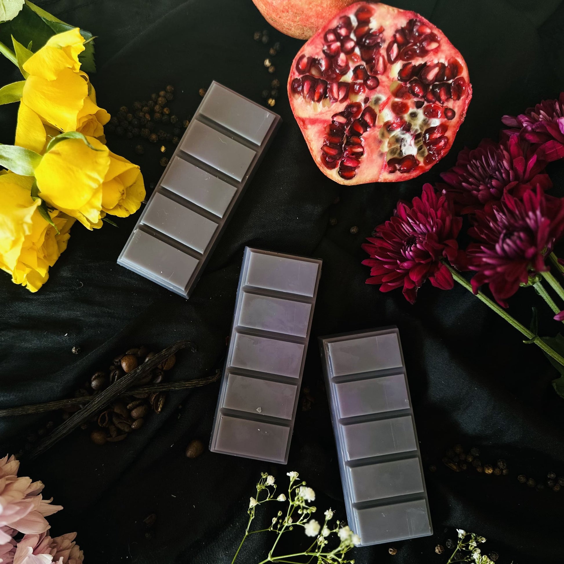 Luxurious purple soy wax melts surrounded by coffee beans, pomegranate and various floral fresh flowers