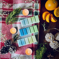 Northern Lights scented snapbar wax melts on a red checked tablecloth surrounded by pinecones, oranges and rosemary
