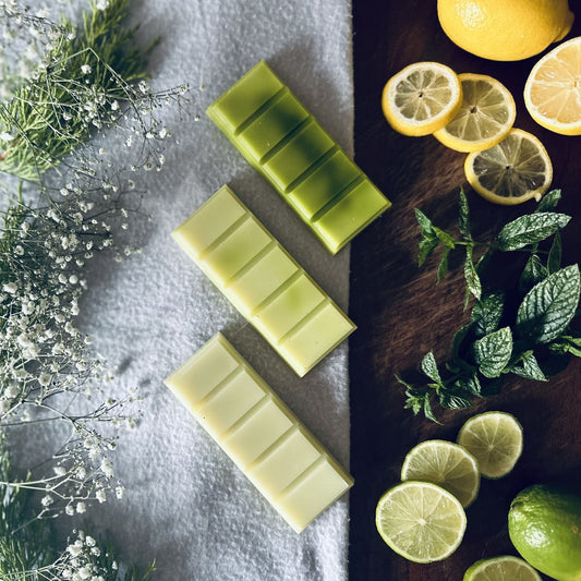 Light and Dark green soy wax melts sitting on a dark oak board surrounded by citrus fruits and mint