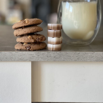 Brown and white soy wax melts sitting next to chocolate chip cookies and a glass of milk