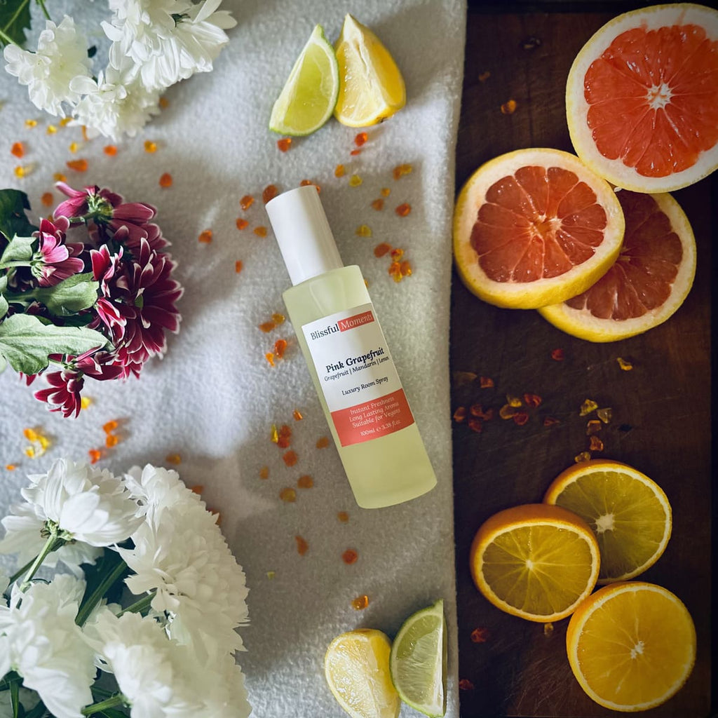 Luxury Pink Grapefruit room spray surrounded by citrus fruits and flowers sitting on a soft cosy blanket.