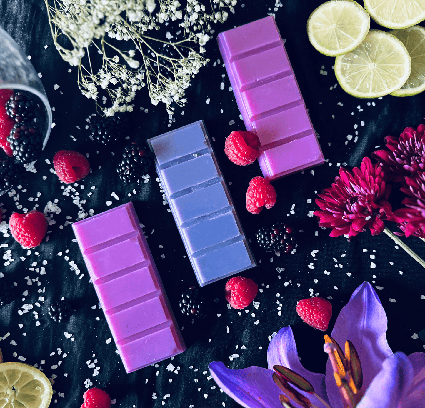 Pink and purple soy wax melts in a luxurious setting surrounded by vibrant flowers and fresh raspberries and blackberries