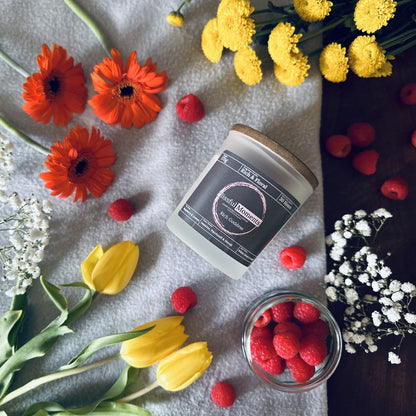 Luxurious perfume scented soy candle surrounded by vibrant orange and yellow tulips with a jar of fresh raspberries