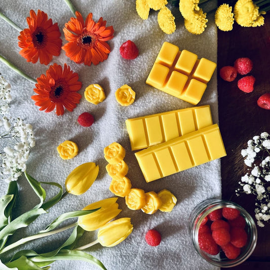 Gold coloured soy wax melts surrounded by fresh yellow and orange tulips with a jar of raspberies