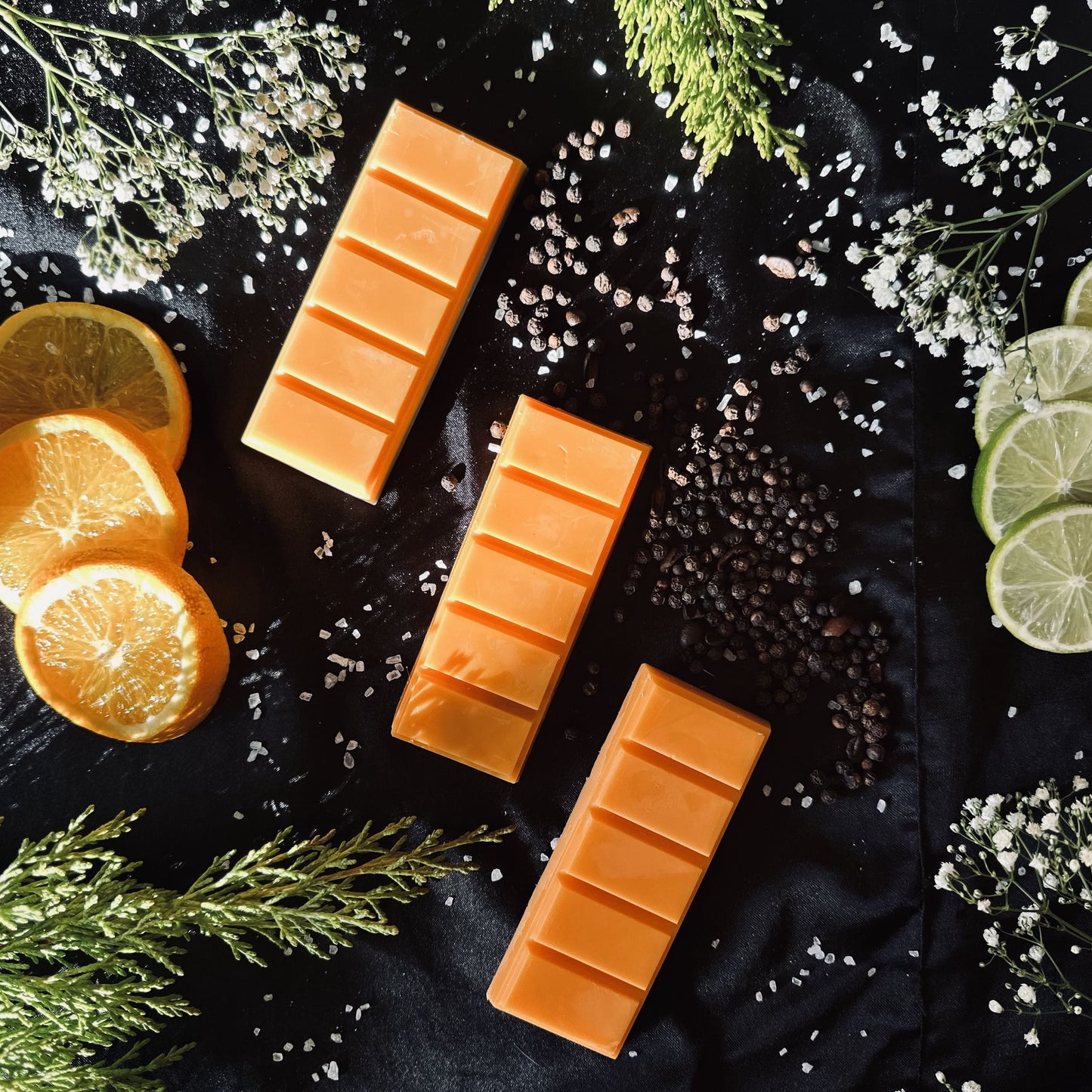 Luxurious aftershave soy wax melts sitting on a bed on peppercorns and surrounded by citrus fruits