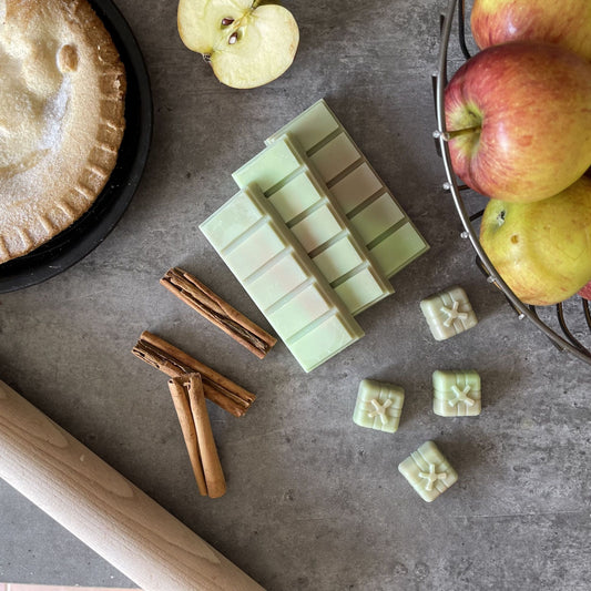 Green soy wax melts in a cosy kitchen setting sitting next to a fresh baked apple pie with red apples and cinnamon sticks next to them