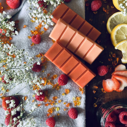 Red and burnt orange soy wax melts in a summer setting surrounded by fresh raspberries and strawberries with white flowers