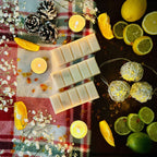 White Christmas snapbar wax melt in a festive decorative setup surrounded with candles, lemons, limes, and string lights on a Christmas checked blanket background.