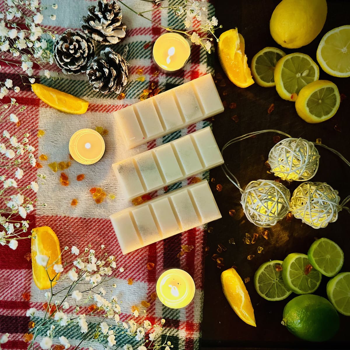 White Christmas snapbar wax melt in a festive decorative setup surrounded with candles, lemons, limes, and string lights on a Christmas checked blanket background.