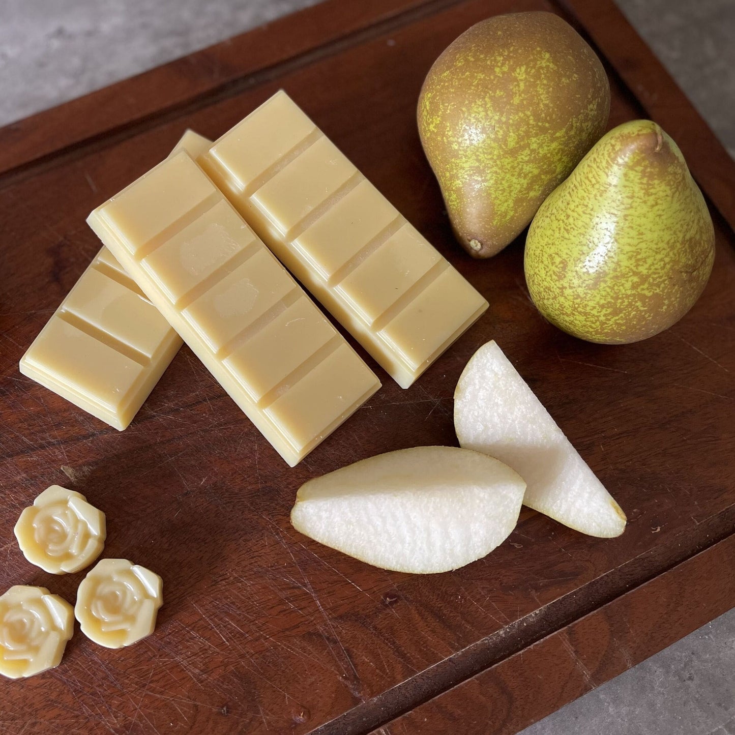 Pear scented soy wax melts on a dark wood board surrounded by pears