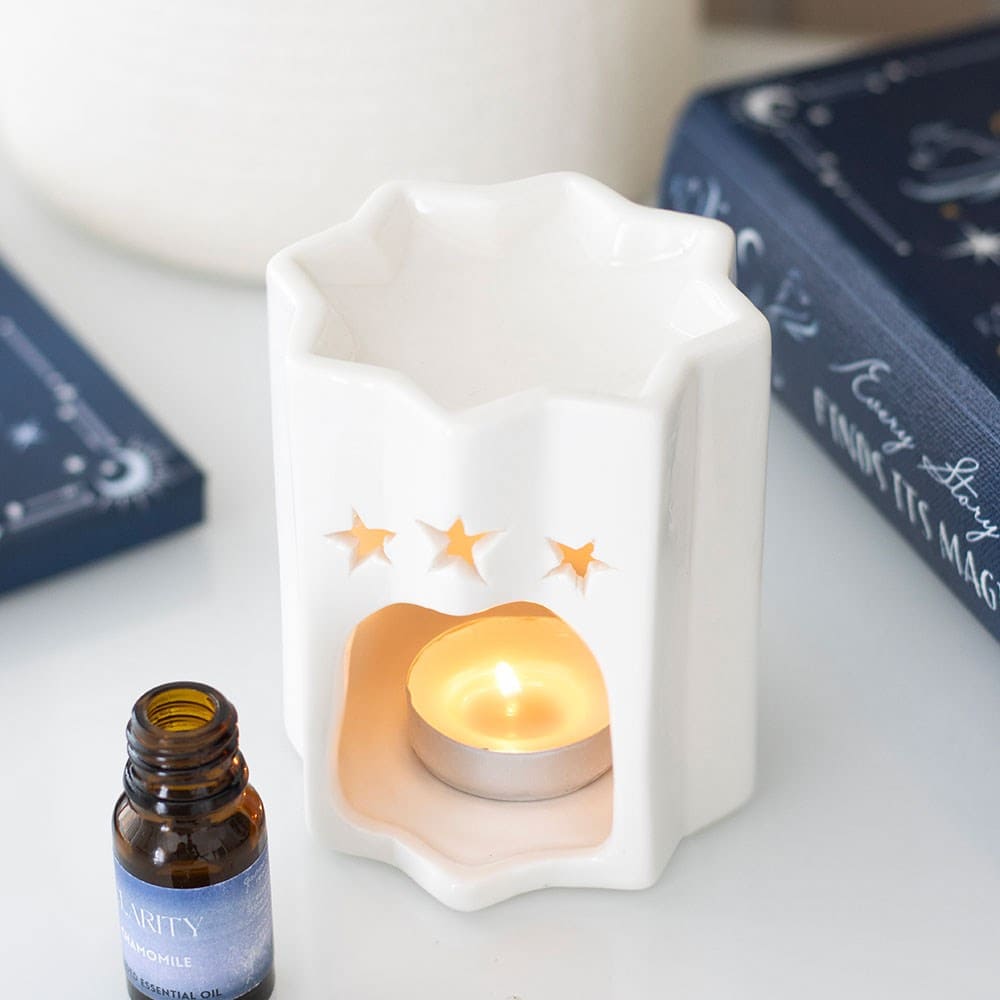 White ceramic wax melt burner shaped as a star with a lit candle inside, surrounded by books