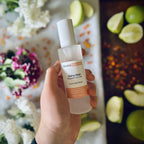 Hand holding Fairy Dust scented luxury frosted glass room spray surrounded by fresh flowers, amber and green apples