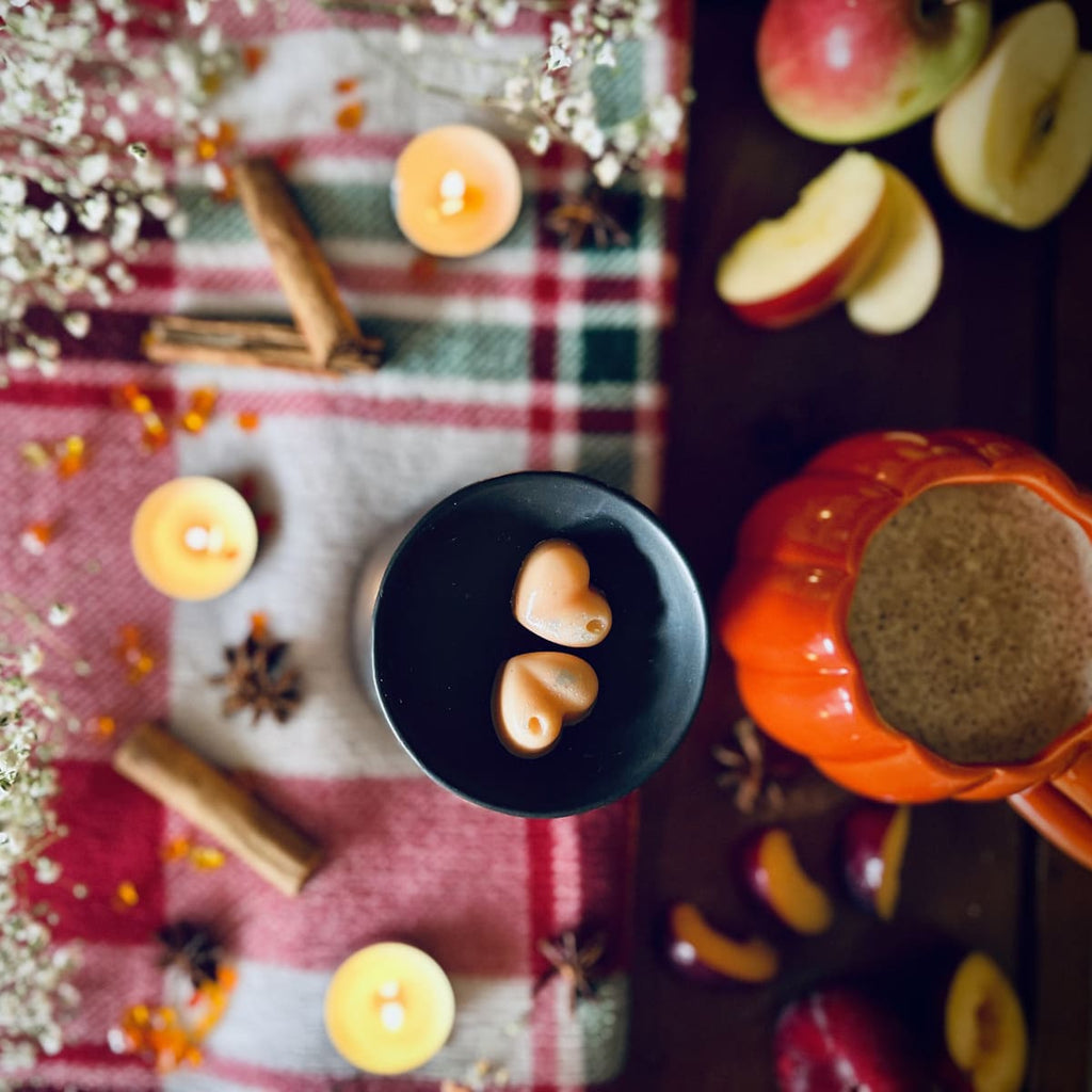 Orange Frosted Pumpkin scented heart shaped wax melts in a black wax melt burner dish on a red plaid tablecloth with apples and candles.