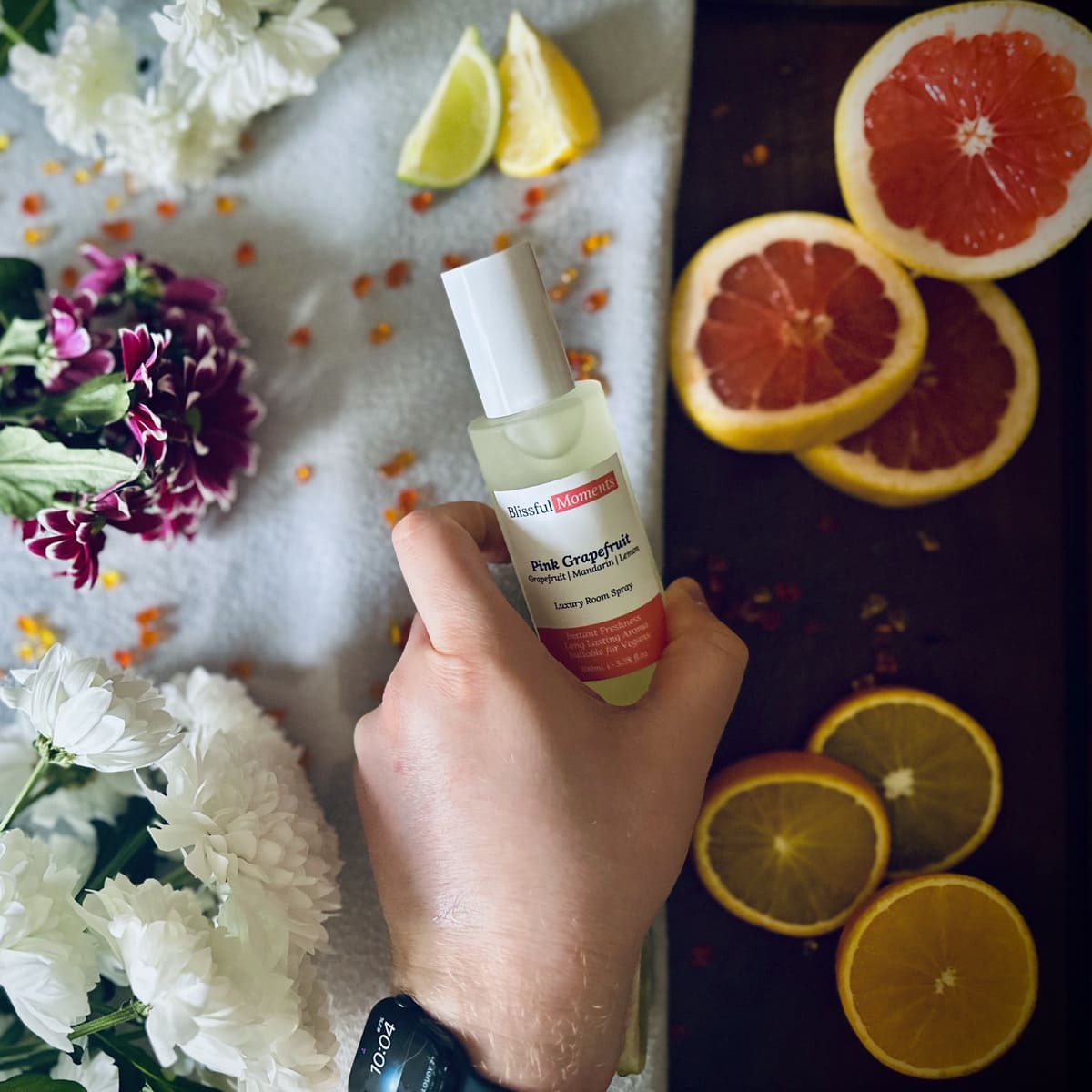 Hand holding a luxury Pink Grapefruit frosted glass room spray surrounded by citrus fruits and flowers