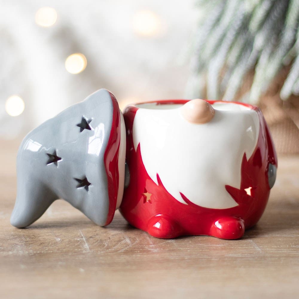 Santa styled Red gnome Gonk wax melt burner with a grey hat lid laying next to the body on a wooden surface with a Christmas background setting