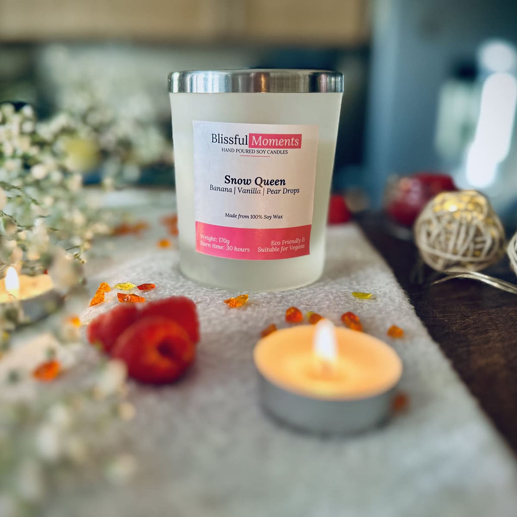 Snow Queen candle with a silver lid on a grey blanket surrounded flowers, tea lights and raspberries