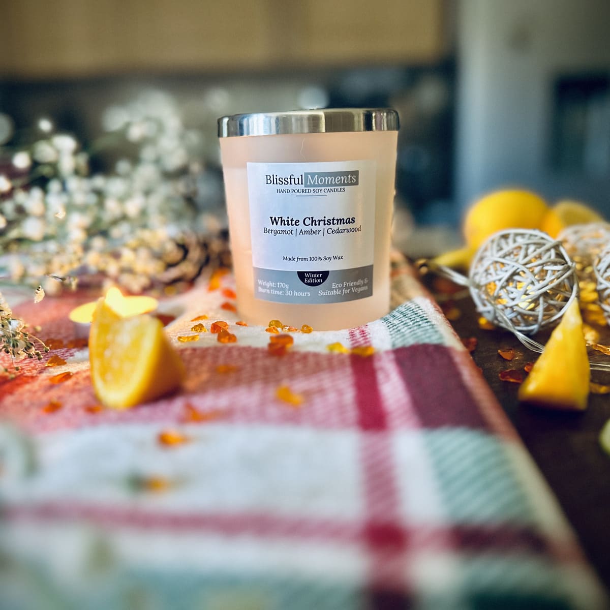 White Christmas scented soy candle on a red checked tablecloth with decorative Christmas items. 