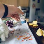 Hand holding Beach House scented luxury frosted glass room spray surrounded by fresh flowers, amber and lemon