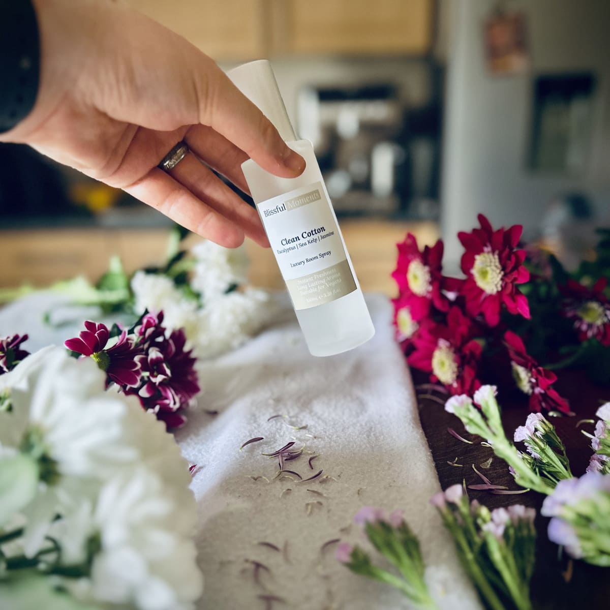 Hand holding a luxury Clean Cotton scented room spray surrounded by fresh flowers.