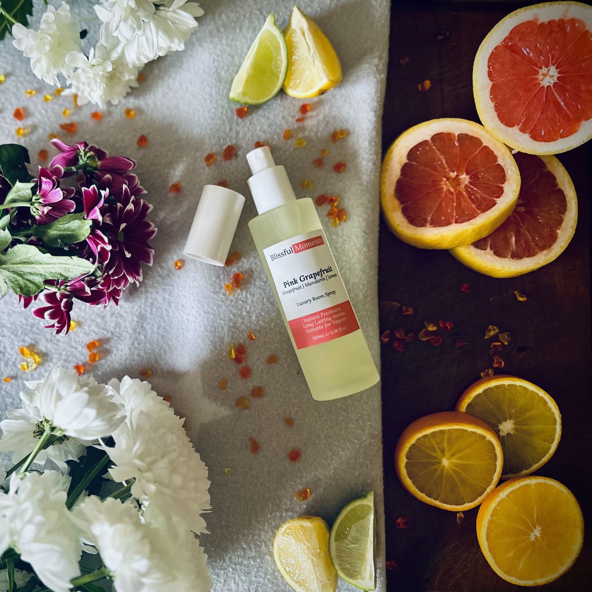 Luxury Pink Grapefruit room spray surrounded by citrus fruits and flowers sitting on a soft cosy blanket.