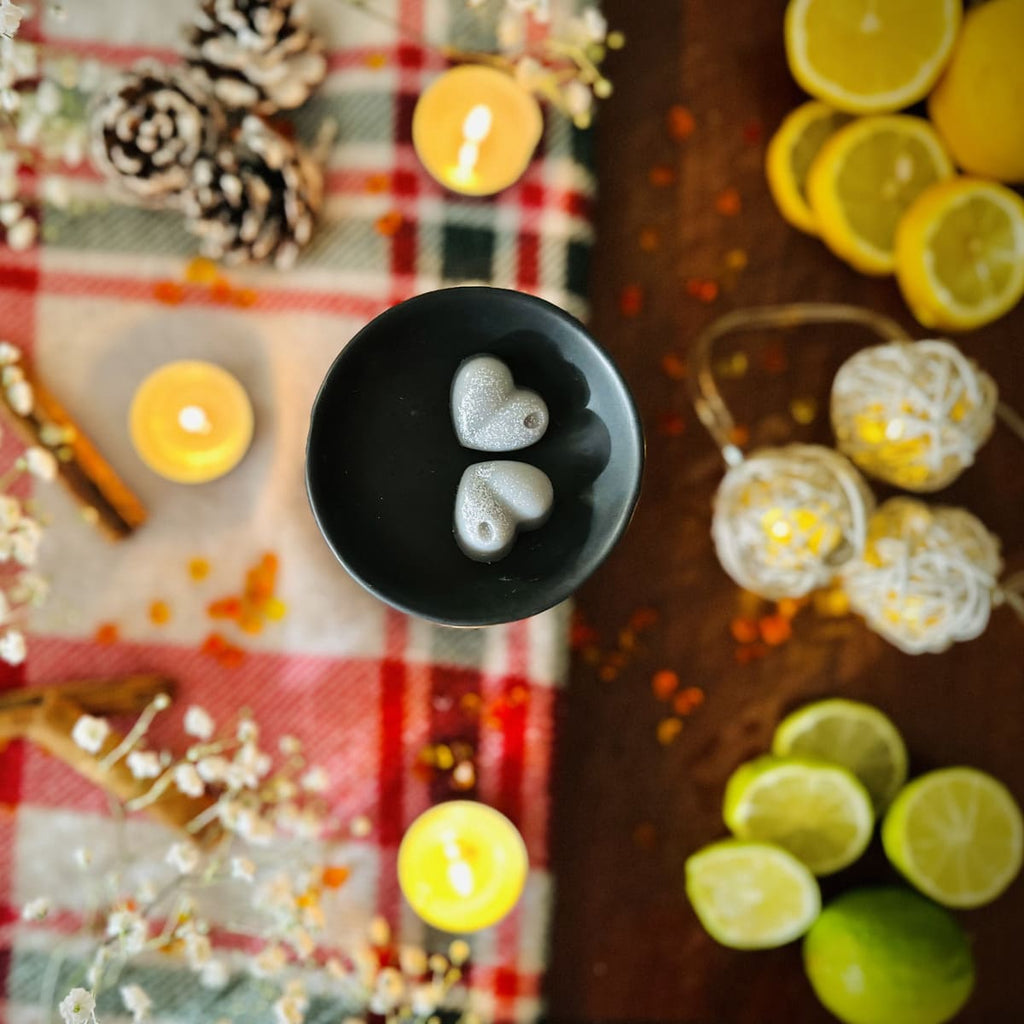 Grey Starry Night heart shaped wax melts with a Christmas decorative setup with candles, pinecones, and citrus fruits on a checkered cloth.