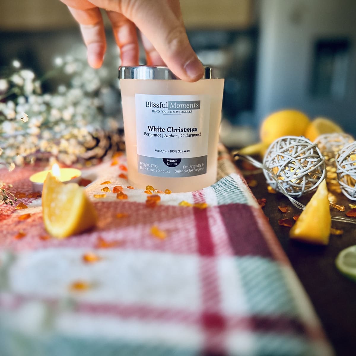White Christmas scented soy candle with a handing the silver lid surrounded by decorative Christmas items