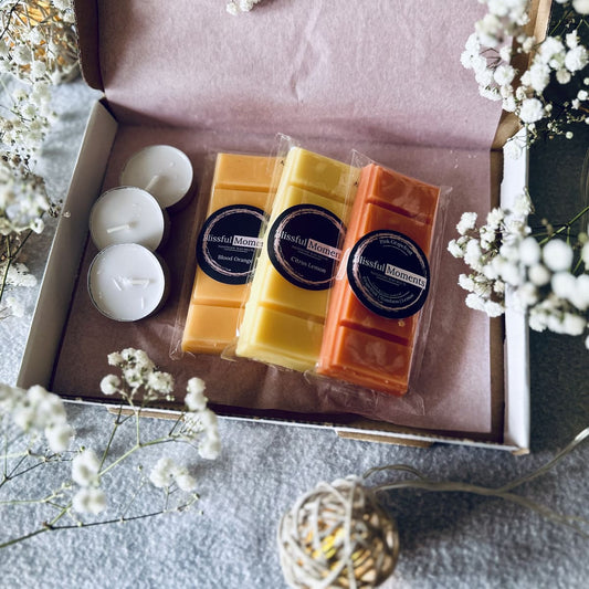 orange, yellow and pink citrus scented soy wax melts in a nicely presented gift box next to tea lights