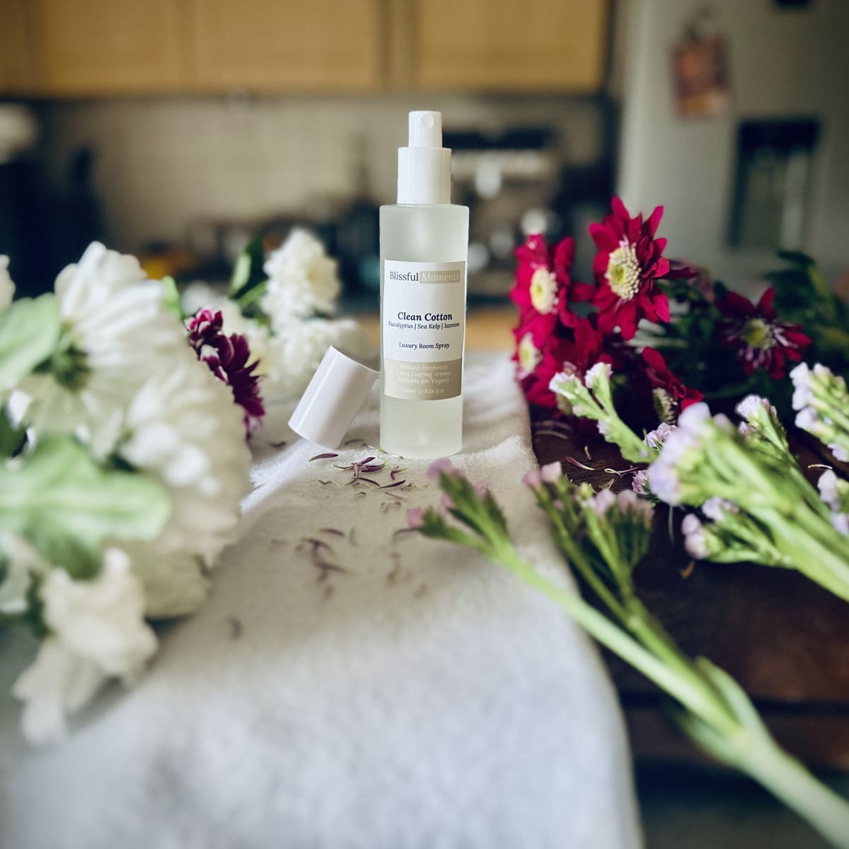 Luxury Clean Cotton scented room spray sitting on a soft cosy blanket surrounded by fresh flowers.