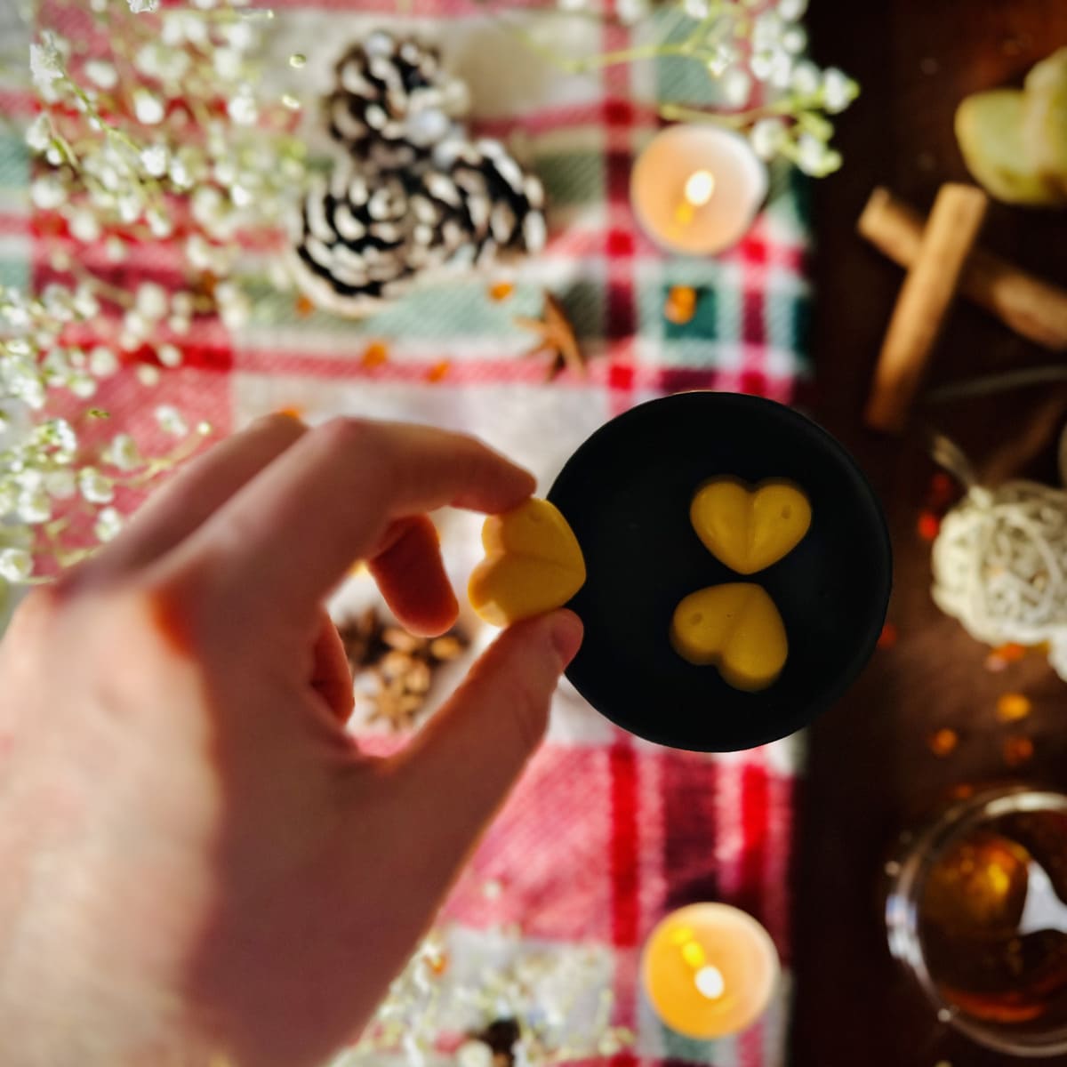 Hand placing Gingerbread scented heart shaped wax melts into a black tealight burner dish with a Christmas decorative background.