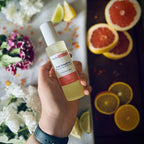 Hand holding a luxury Pink Grapefruit frosted glass room spray surrounded by citrus fruits and flowers