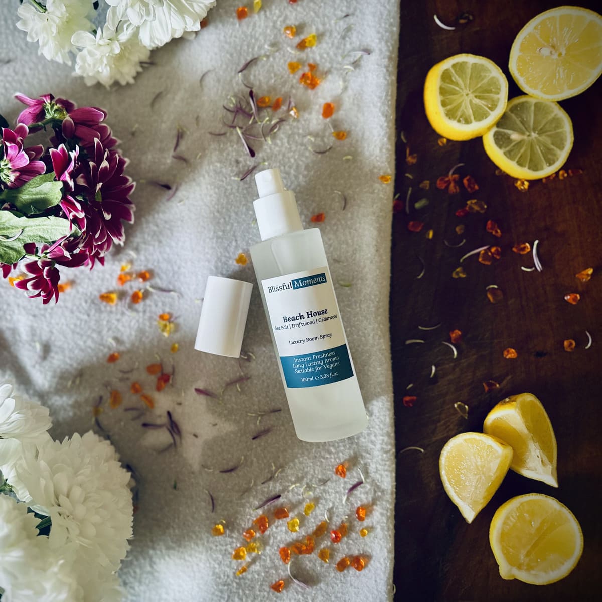 Beach House scented luxury frosted glass room spray surrounded by fresh flowers, amber and lemon sitting on a cosy blanket